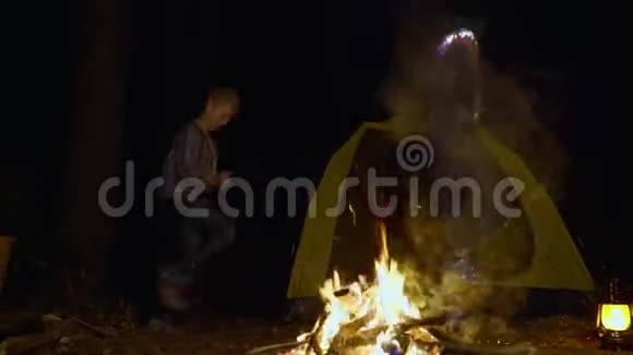 青少年男孩和女孩在夜间森林的露营地篝火旁跳舞快乐的旅游青年在篝火旁跳舞视频的预览图