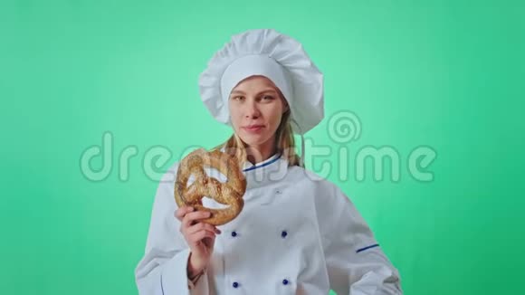 兴奋的面包师带着一张漂亮的脸在绿色的工作室里贪婪地吃着一个新鲜的椒盐卷饼看上去很吸引镜头视频的预览图