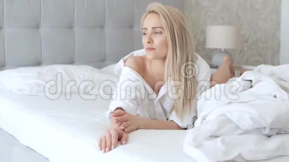 美丽的中年妇女躺在床上穿着白色衬衫微笑着视频的预览图