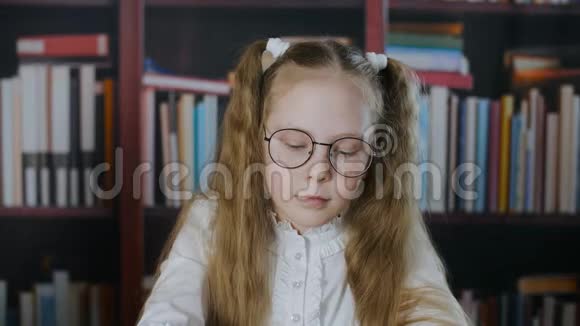 肖像女学生戴着圆形眼镜两条发尾在书架背景上书架上戴眼镜的女学生视频的预览图
