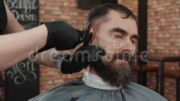 在理发店用理发机和梳子剪头发的留着胡子的人理发师用发型视频的预览图