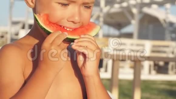 可爱的男孩在度假时在海滩上吃成熟的新鲜西瓜视频的预览图
