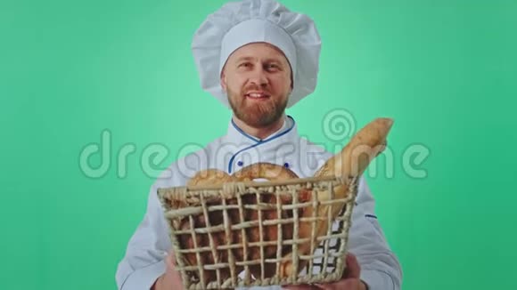 在一个绿色的工作室里一个面包师大个子男人微笑着手里拿着一个装满新鲜面包的大篮子直视着摄像机视频的预览图