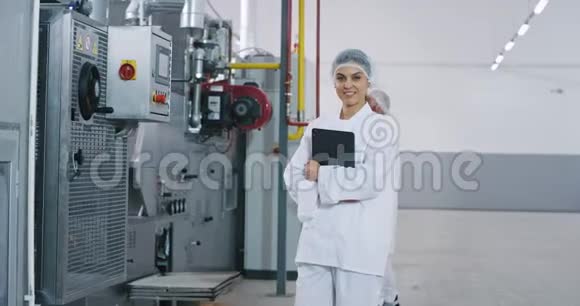一位漂亮的工程师女士在一个拥有电子平板电脑的大型制造业中她带着完美的微笑视频的预览图