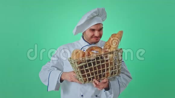 在一个绿色的工作室里微笑着大面包师拿着一篮子新鲜面包闻着面包的味道然后直视着视频的预览图