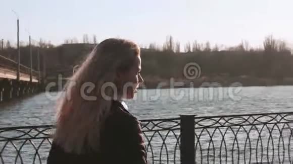 阳光明媚的日子美丽的年轻女子在城市的河堤上散步视频的预览图