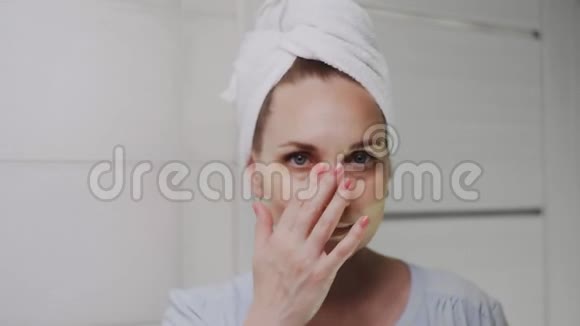 一位头上戴着毛巾的成年女士将胶原蛋白垫放在眼睛下面看着镜头视频的预览图