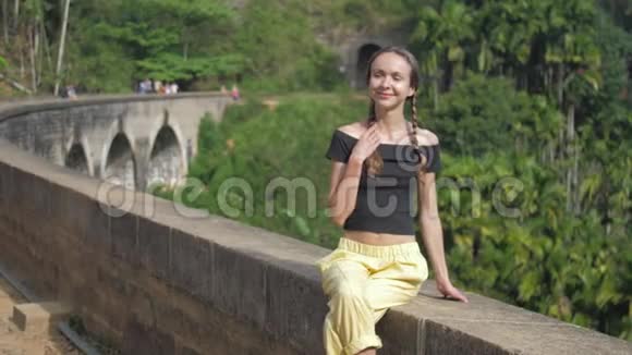 穿着黑色上衣的女孩坐在老桥上对着森林微笑视频的预览图