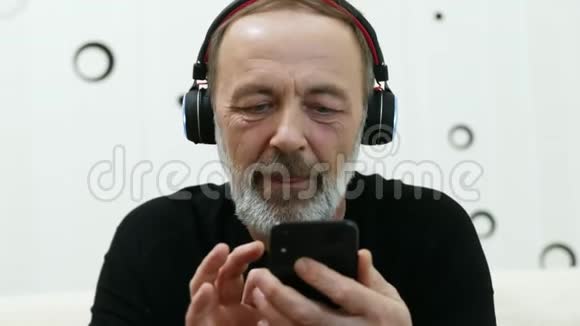 无线耳机中的中年男子欣赏音乐的肖像在手机上搜索新音乐视频的预览图