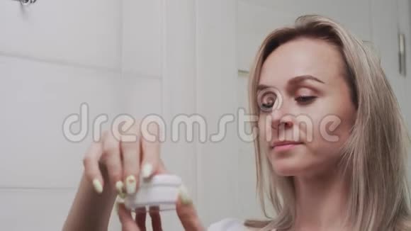 女人在眼睛下面涂上奶油照镜子享受自然的美丽和健康视频的预览图