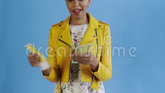 漂亮的美国黑人妇女正在用蓝色背景的黄色夹克数钱视频的预览图