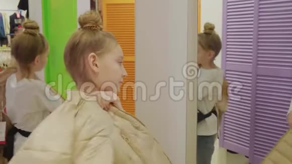 年轻女孩在时装陈列室购物时试着用米色夹克前镜年轻女孩在寻找新的镜子视频的预览图