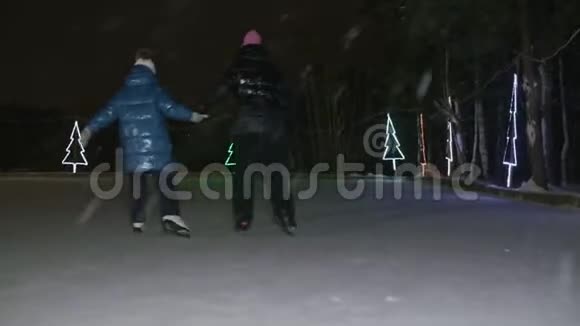 晚上带孩子在冰上滑冰的母亲的后景视频的预览图