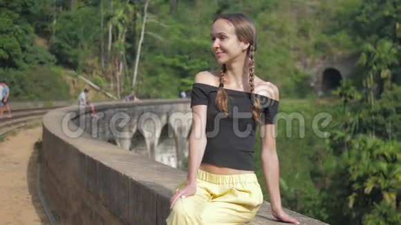 女孩坐在历史桥上微笑着面对野生森林视频的预览图