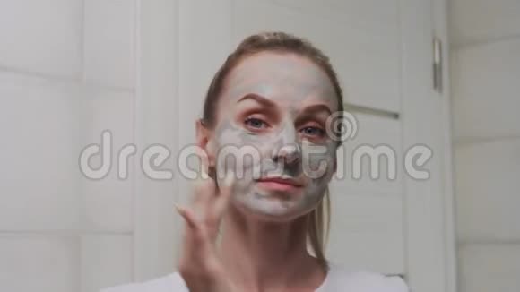 靠近女人在她的脸上涂上粘土面具看着相机视频的预览图