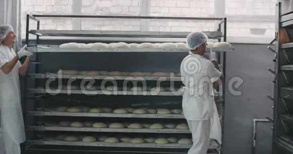两个专业的面包店工人穿着白色制服从货架上卸下所有的生面包准备好运送面包视频的预览图