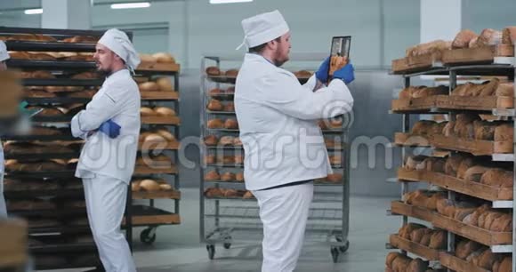 主面包师用一种新技术平板电脑从货架上拍照其他两名工人在发言视频的预览图