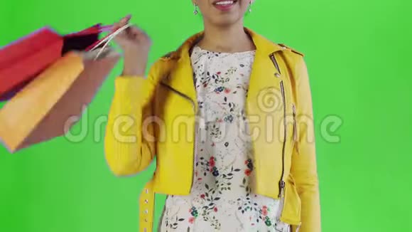 美国黑人妇女在工作室绿色背景上带购物袋的肖像幸福的女人手里拿着视频的预览图