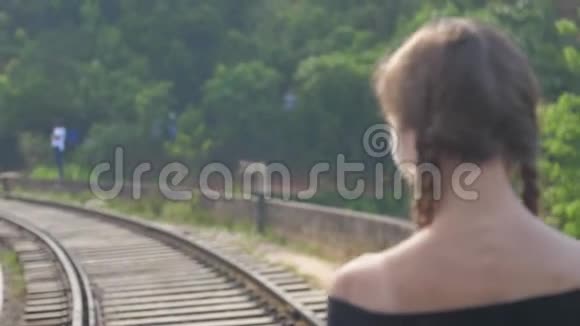 穿着黑色上衣的女孩走在丛林中的老铁路小径上视频的预览图