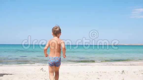 快乐的小男孩沿着海滩向大海跑去视频的预览图