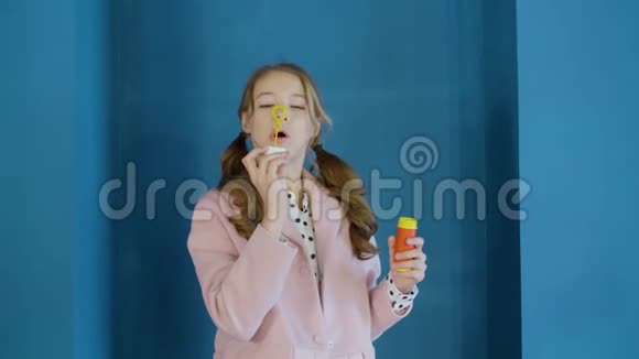 快乐的少女在蓝墙背景的工作室吹肥皂泡带着两头卷发的女学生视频的预览图