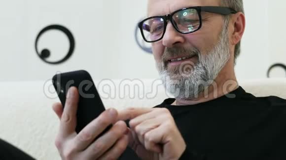 留着灰胡子戴着眼镜的中年潮人在家里用手机特写视频的预览图