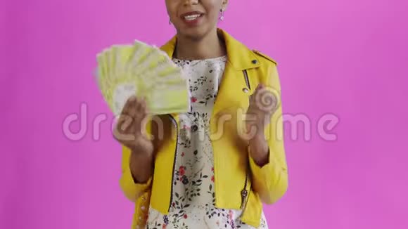 满意的兴奋的兴奋的非裔美国妇女在粉红色的背景上说YEAH黄色的夹克视频的预览图