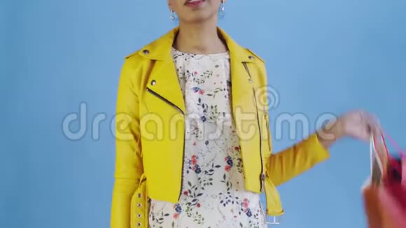 非洲裔美国妇女的肖像与购物袋和黄金信用卡在蓝色背景在工作室黄色夹克视频的预览图