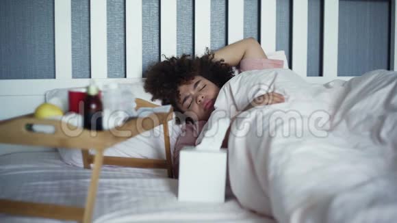 生病的非洲裔美国女孩在床上用湿巾擤鼻子视频的预览图
