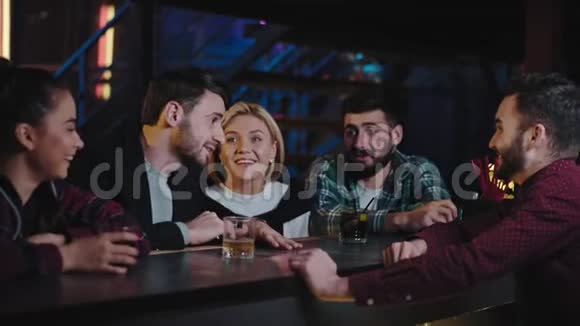 很有吸引力的一群年轻的微笑的大朋友在现代酒吧里享受夜晚的时光同时喝了一些视频的预览图