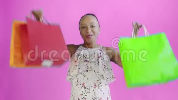 一位非洲裔美国妇女的画像在摄影棚里用粉色背景的购物袋跳舞幸福女人抱视频的预览图