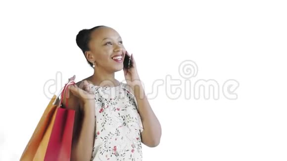 年轻美丽的非洲人使用电话和拿着购物袋在白色背景在工作室带花的白色裙子视频的预览图