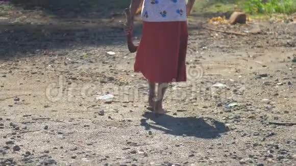 穿着短裙拿着弯刀的老妇人沿着肮脏的道路行走视频的预览图