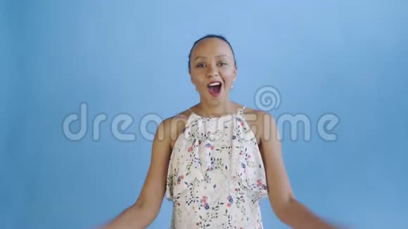 满意的高兴兴奋的非裔美国妇女显示金钱和说我的上帝在蓝色背景白色连衣裙视频的预览图