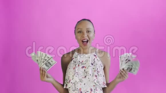 满意高兴兴奋非洲裔美国妇女展示钱说我的上帝在粉红色背景白色礼服与视频的预览图