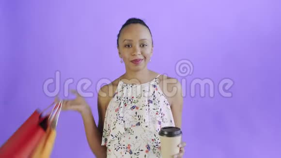 画室里一位拿着购物袋的非裔美国妇女正在喝紫色背景的咖啡JWhite连衣裙视频的预览图