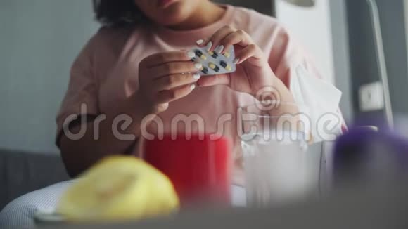 一个生病的非裔美国女孩躺在沙发上用水吃药视频的预览图