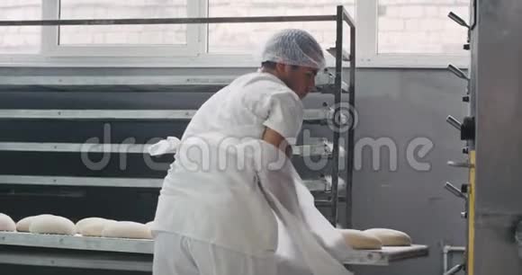 面包业的两名工人把生面包装进烤箱机进行烘烤他们穿着特殊的白色衣服视频的预览图