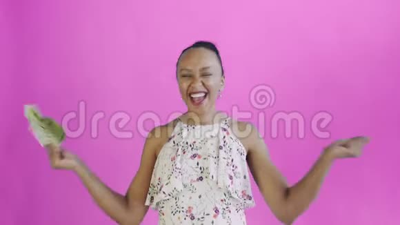 满意高兴兴奋非洲裔美国妇女显示金钱并说YEAH在粉红色背景白色连衣裙视频的预览图