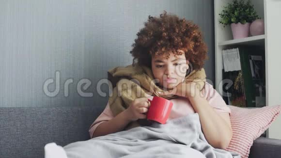 一位年轻的非裔美国女孩正在喝热茶她咳嗽喉咙痛用毯子裹着身体视频的预览图
