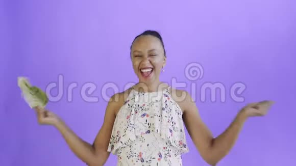 满意快乐兴奋的非洲裔美国妇女在紫色背景下展示金钱并说是白色连衣裙视频的预览图
