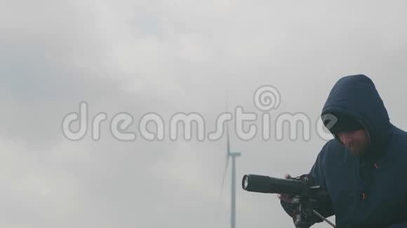 一个职业胡子摄影师在一个多云的天气站在一个旋转的风力发电机和从一个视频的预览图