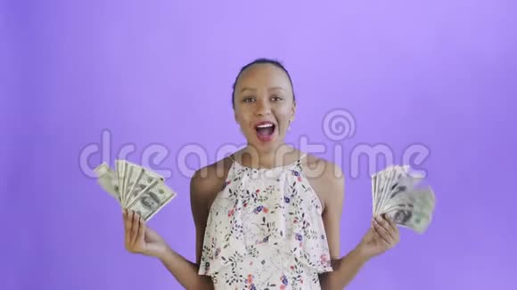 满意高兴兴奋非洲裔美国妇女展示钱说我的上帝在紫色背景白色礼服与视频的预览图