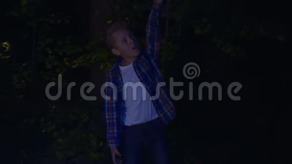男孩拿着手电筒在头顶上方晚上在黑暗的森林里散步视频的预览图
