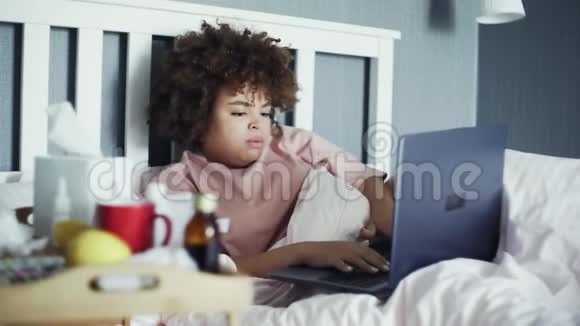 病态自由职业者非洲裔美国女孩患流感躺在床上用笔记本工作视频的预览图
