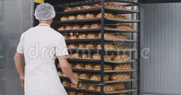 烘焙面包装入工业烤箱的过程中烘焙工人在他旁边的大架子上装载食物视频的预览图