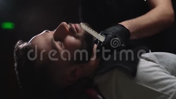 戴黑手套的男理发师剃胡子的客户视频的预览图
