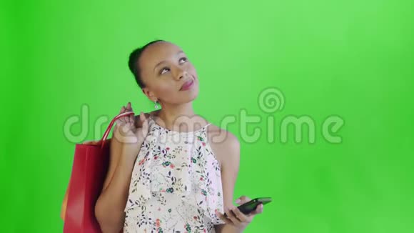 年轻漂亮的非洲人在录音室里用手机拿着绿色背景的购物袋带花的白色连衣裙视频的预览图
