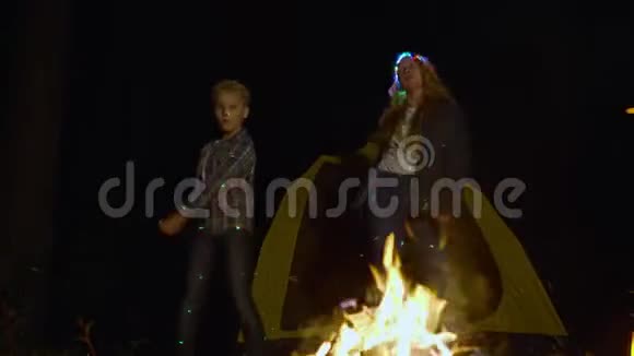 快乐的男孩和女孩在夜间林地的露营地篝火旁跳舞游客在篝火旁跳舞视频的预览图