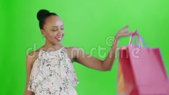 一位非洲裔美国妇女正在摄影棚里摆着绿色背景的购物袋快乐女人购物五彩缤纷视频的预览图